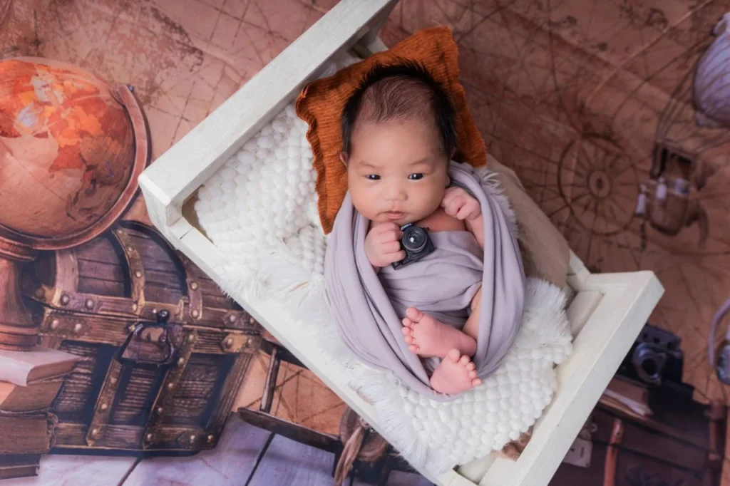 Newborn baby wrapped in a lavender blanket posed in a small white bed prop