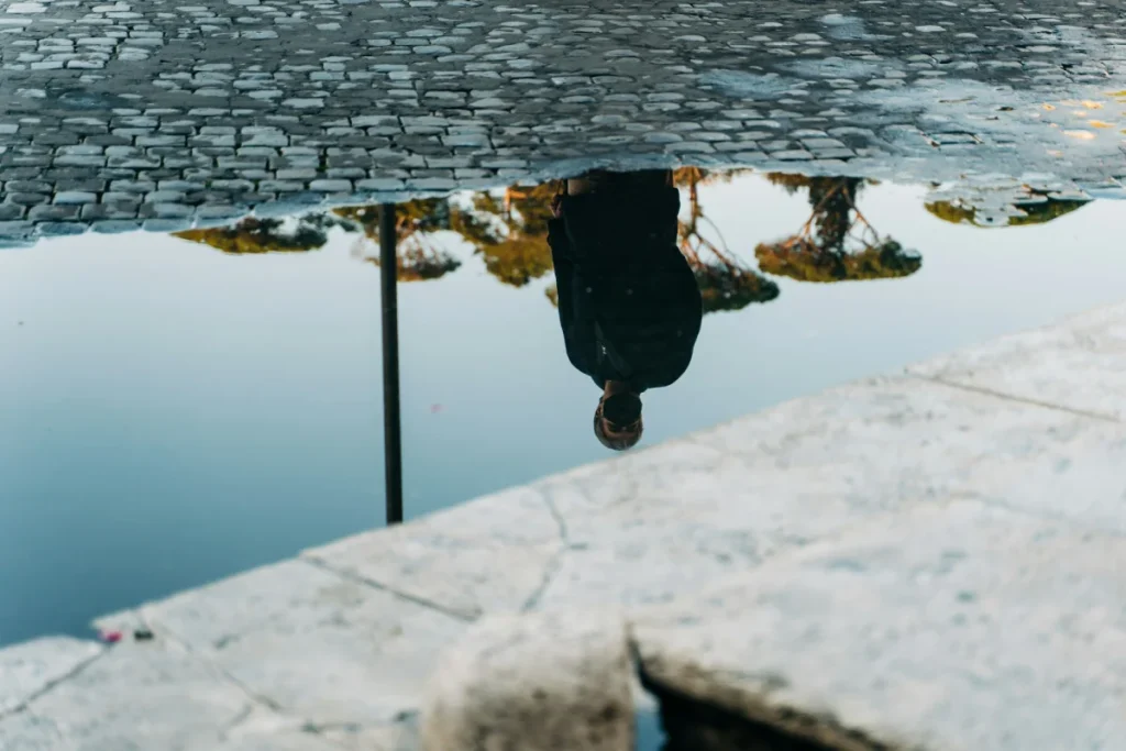 Person reflected upside down in still water beside a stone edge