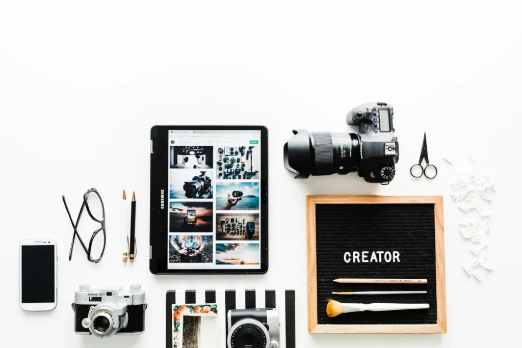 Flat lay of a camera, tablet showing photos and creator tools on a white desk