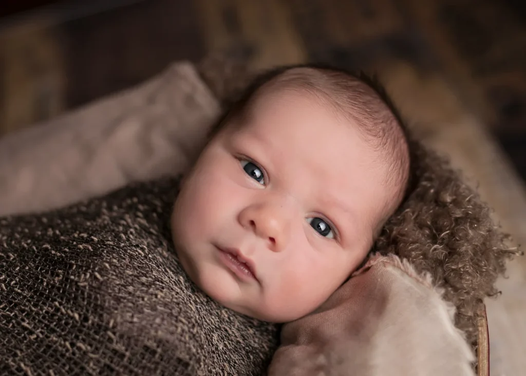 Newborn baby lying on a textured blanket looking at the camera