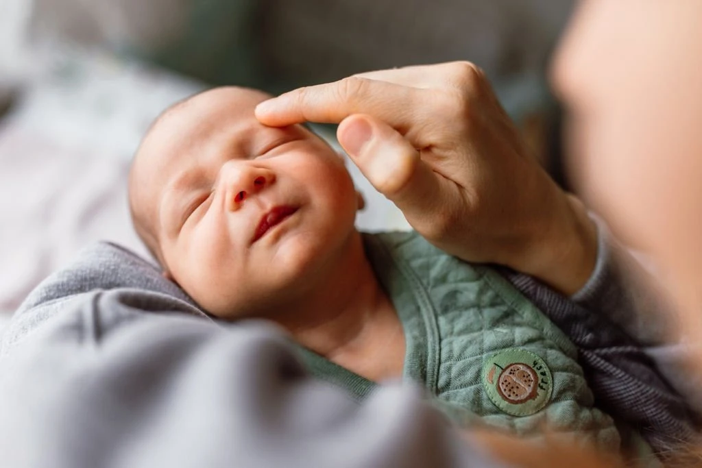 Parent's hand gently touching a sleeping newborn's face