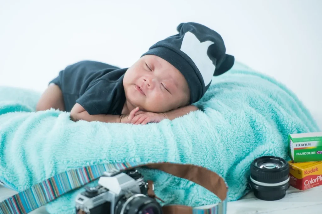 Newborn sleeping on a blue blanket with a camera and lens beside them
