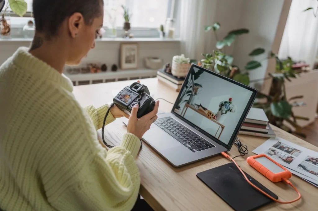 Photographer editing photos on a laptop while holding a camera